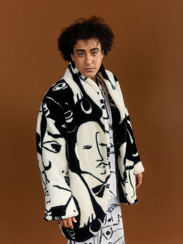 Adam El Mouna portant un manteau de fausse fourrure à motifs de visages noir et blanc