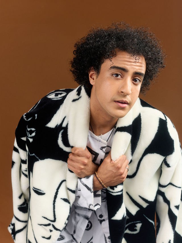 Adam El Mouna resserrant son manteau imprimé sur ses épaules